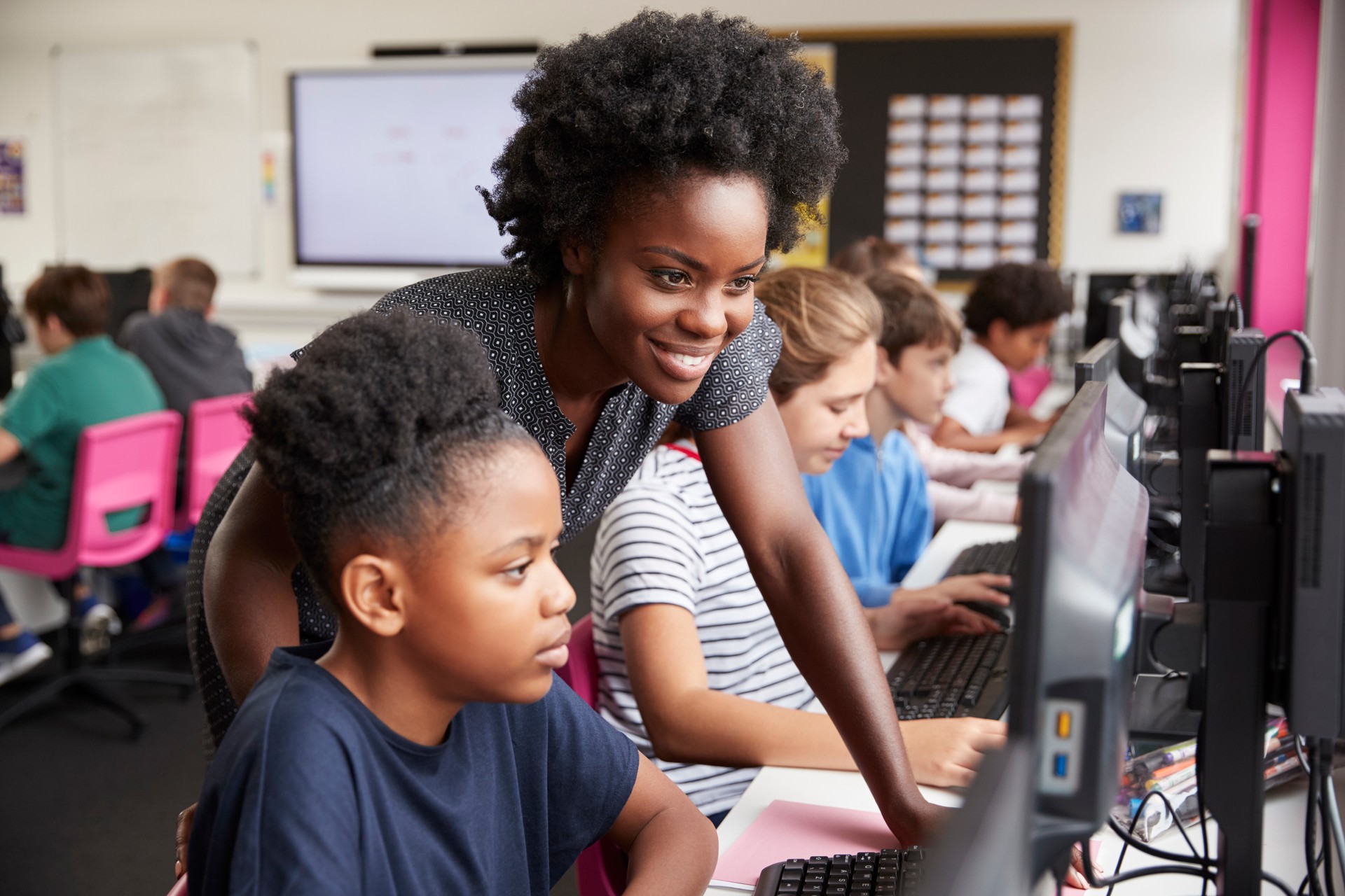 Top View Shot in Elementary School Computer Science Classroom: Children Sitting at their School Desk Using Personal Computers and Digital Tablets for Assignments.